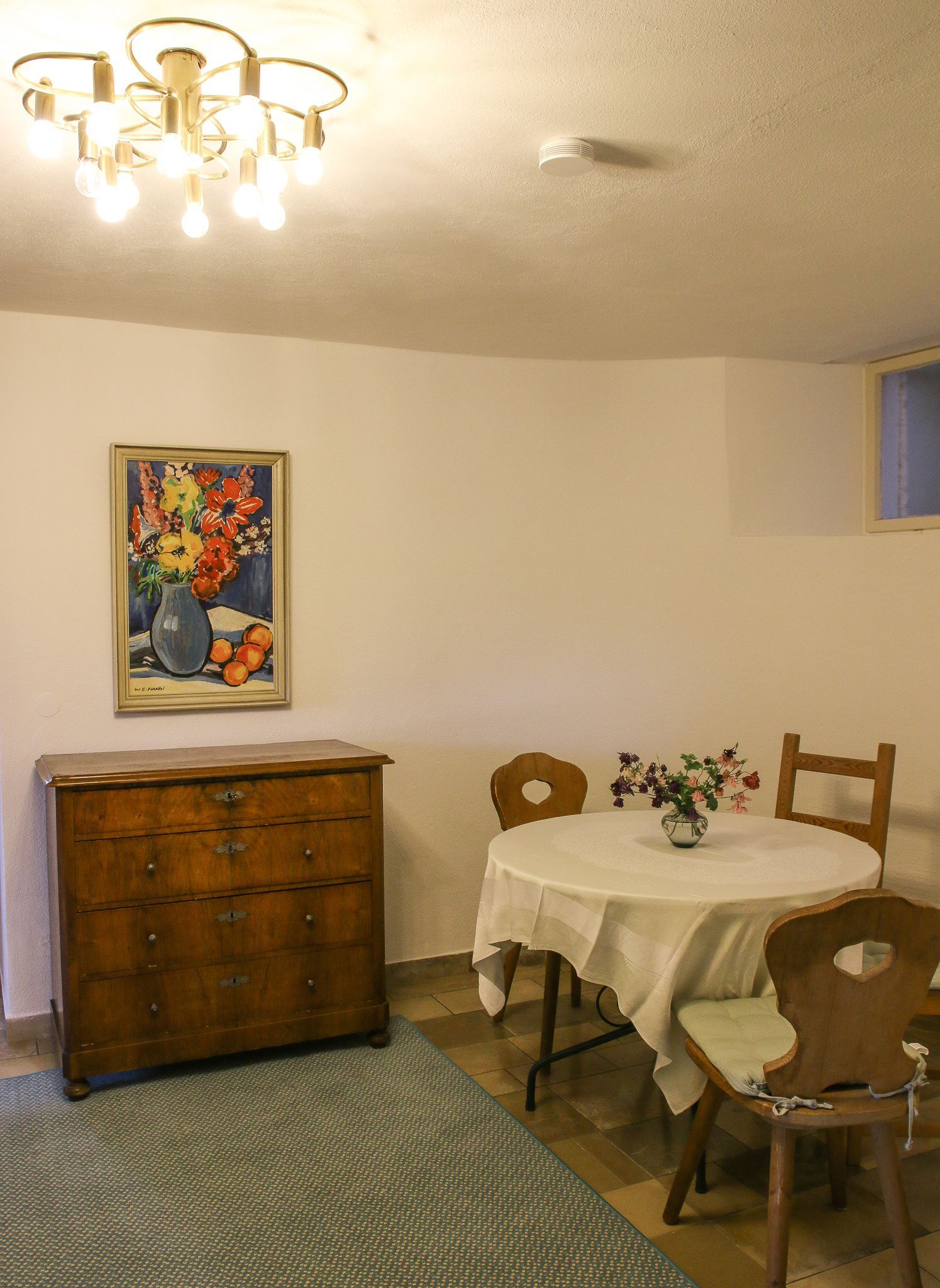 Een eethoek met een tafel, stoelen, een houten kast, een schilderij en een plafondlamp.