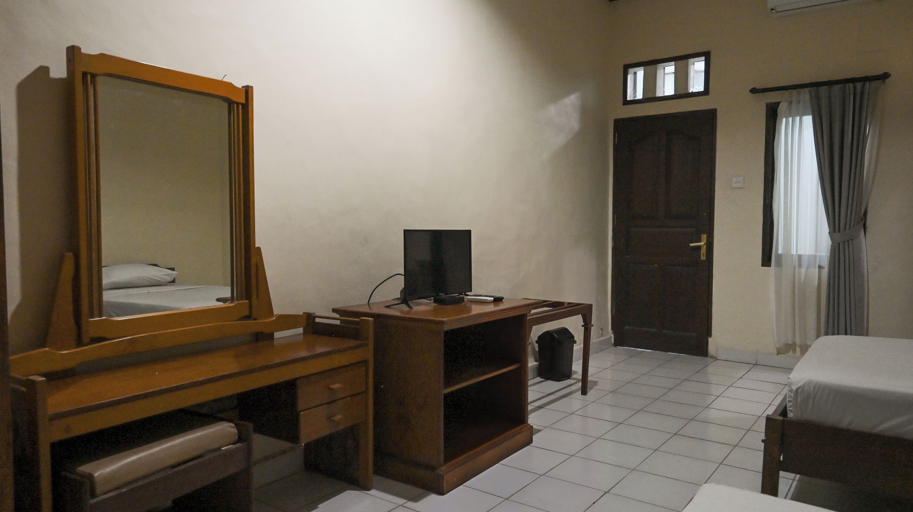 Hotelkamer met een houten bureau, een grote spiegel, een bed, een deur en een raam met gordijnen.
