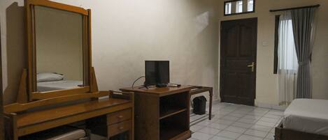 A hotel room with a wooden desk, a large mirror, a bed, a door, and a window with curtains.