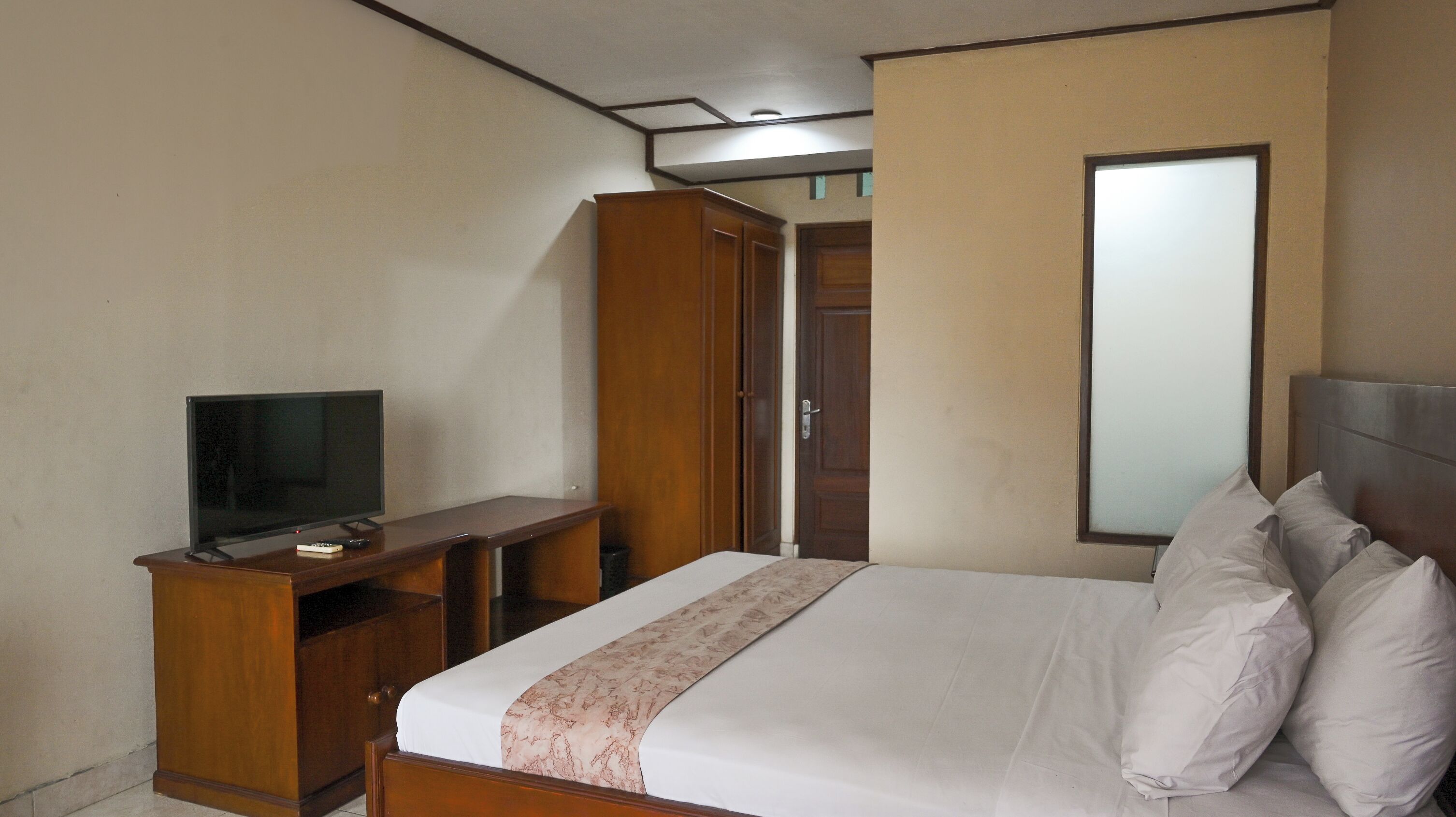 A hotel room with a bed, a TV on a wooden stand, a wardrobe, and a mirror on the wall.
