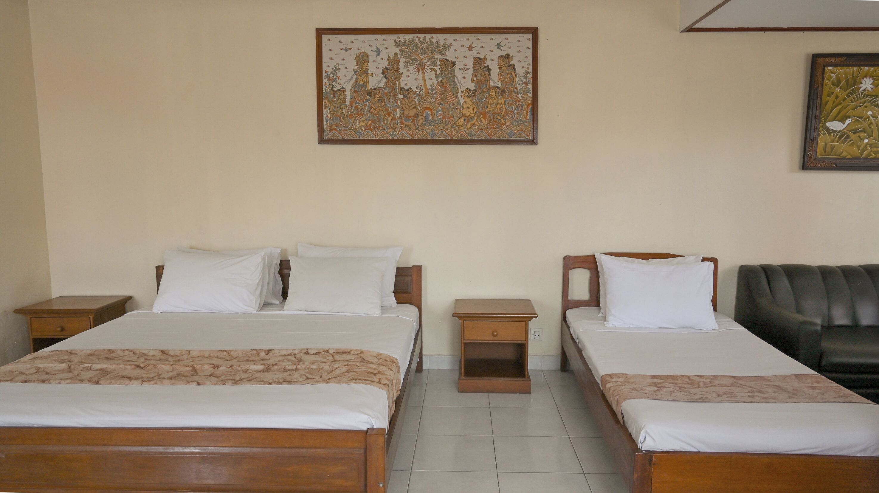 A hotel room with two beds, a wooden headboard, a nightstand, and a black leather couch.