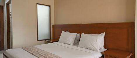 A neatly made bed with white linens and a patterned throw blanket, a wooden headboard, and a nightstand with a drawer.