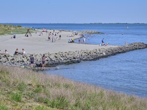 A beach with people, a rocky breakwater, and calm water. - Holiday home in a park with a swimming pool (Baarland)