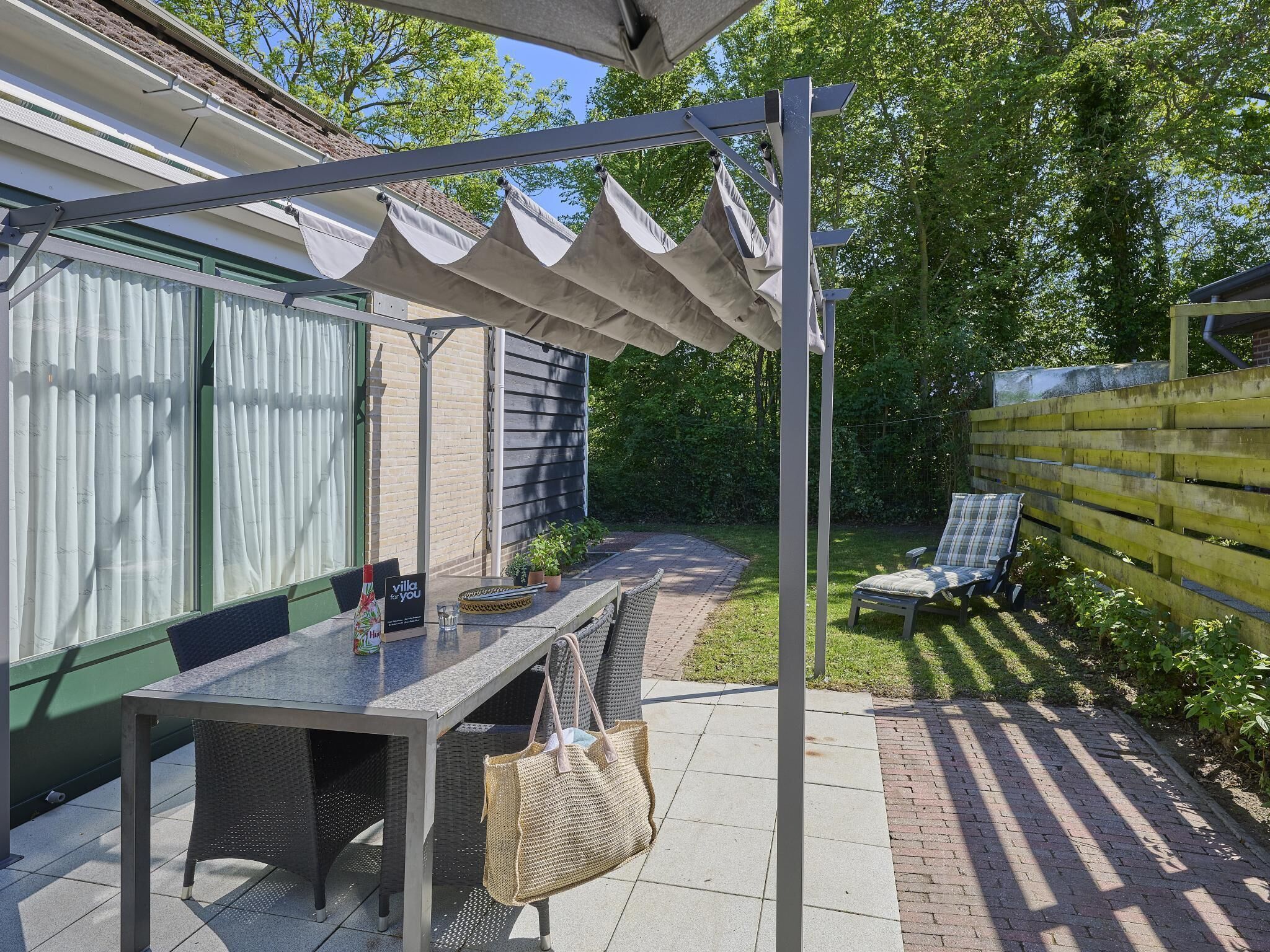 A covered patio with a table and chairs, a hanging chair, and a garden view.