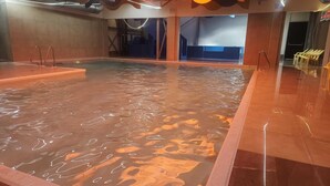 Uma grande piscina interior com design de teto ondulado e chão revestido com azulejos.