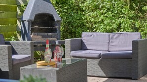 Uma área externa com assentos de vime, uma mesa de vidro e um forno a pizza.