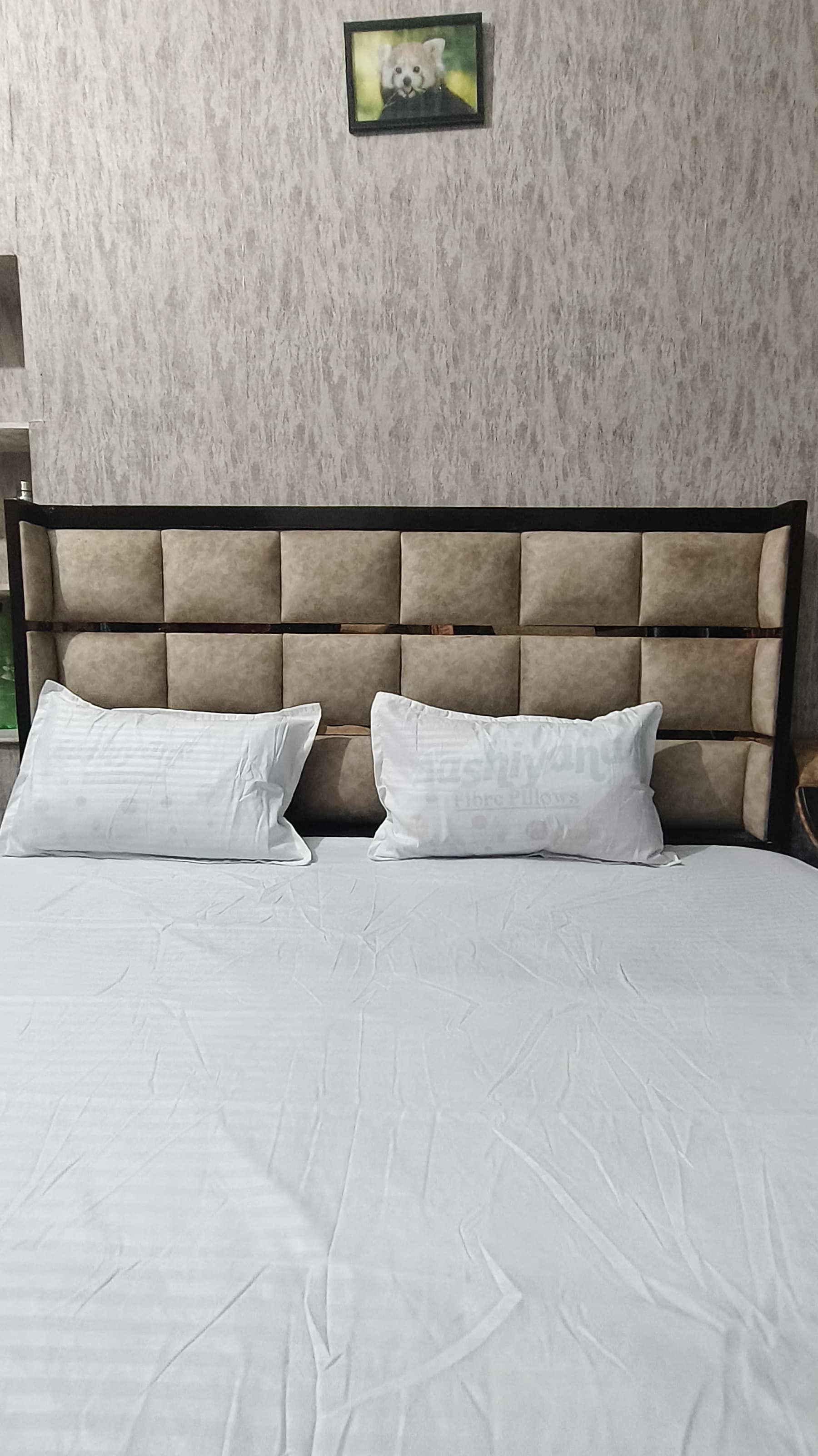 A bed with a headboard, two pillows, and a wall with a framed picture.