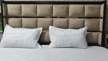 Una cama con cabecera, dos almohadas y una pared con un cuadro enmarcado.