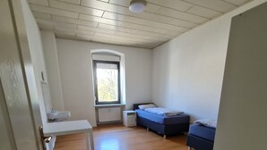 Une pièce avec un plancher en bois, un lit, une petite table et une fenêtre avec des stores.