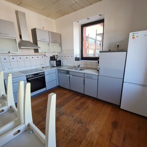 A modern kitchen with white cabinets, a built-in oven, a microwave, and a refrigerator. - Pluwiger Apartments (Pluwig)
