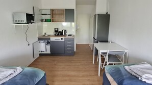 Une chambre d’hôtel compacte comprenant deux lits simples, une petite kitchenette, une table à manger et un espace nuit séparé.