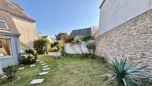 Jardín residencial con un muro de piedra, un pequeño patio y diversas plantas.