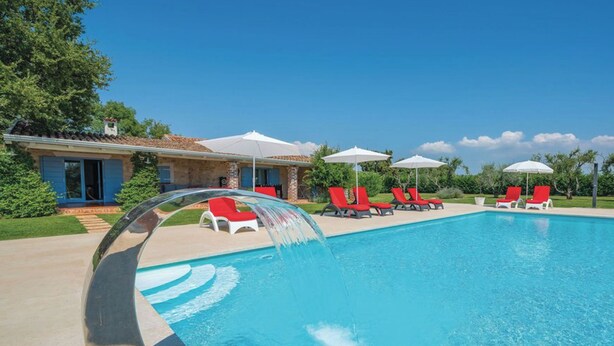 Piscina com um recurso aquático, cadeiras de descanso vermelhas e guarda-sóis.