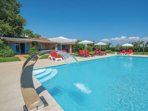 A swimming pool with a water feature, red lounge chairs, and umbrellas. - Green Experience by Interhome (Poreč/Tar)