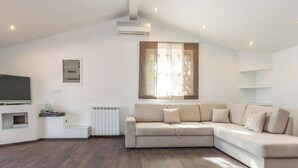 Uma sala de estar moderna com um sofá seccional, uma TV de tela plana, um radiador e uma janela com cortinas leves.