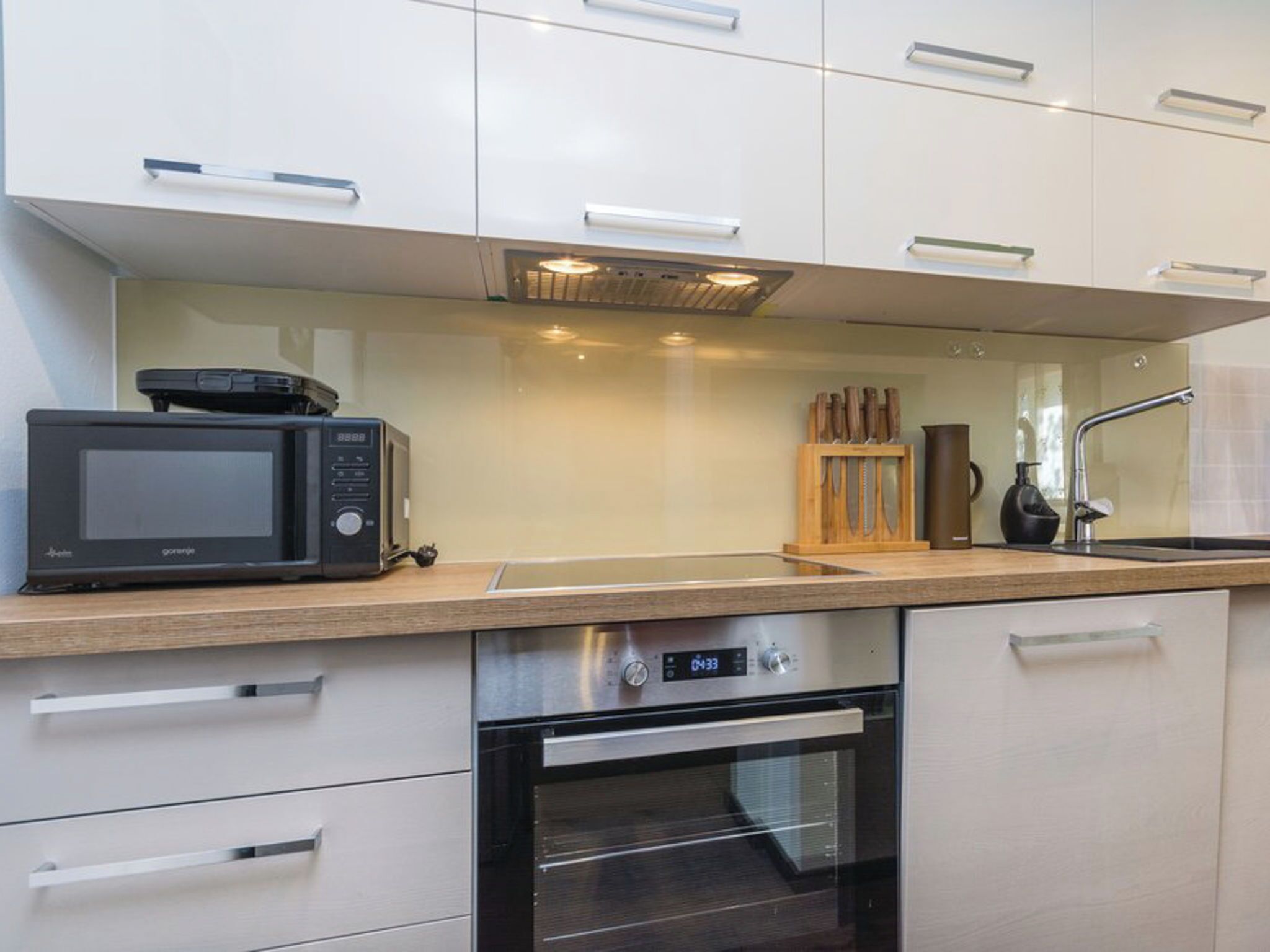 Una cocina moderna con armarios blancos, un microondas, una cafetera y un horno empotrado.
