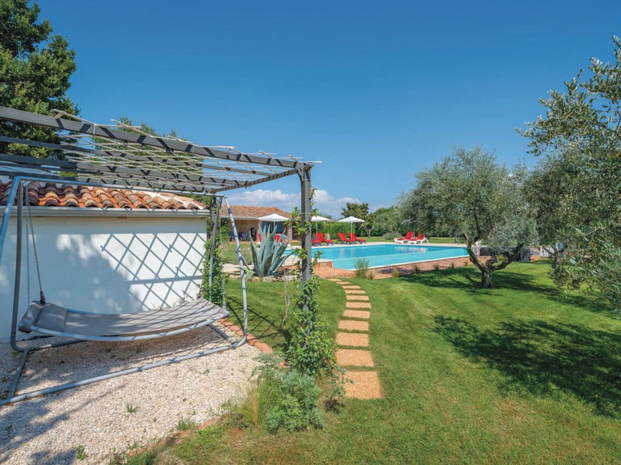 A backyard with a swimming pool, a pergola, and a garden.