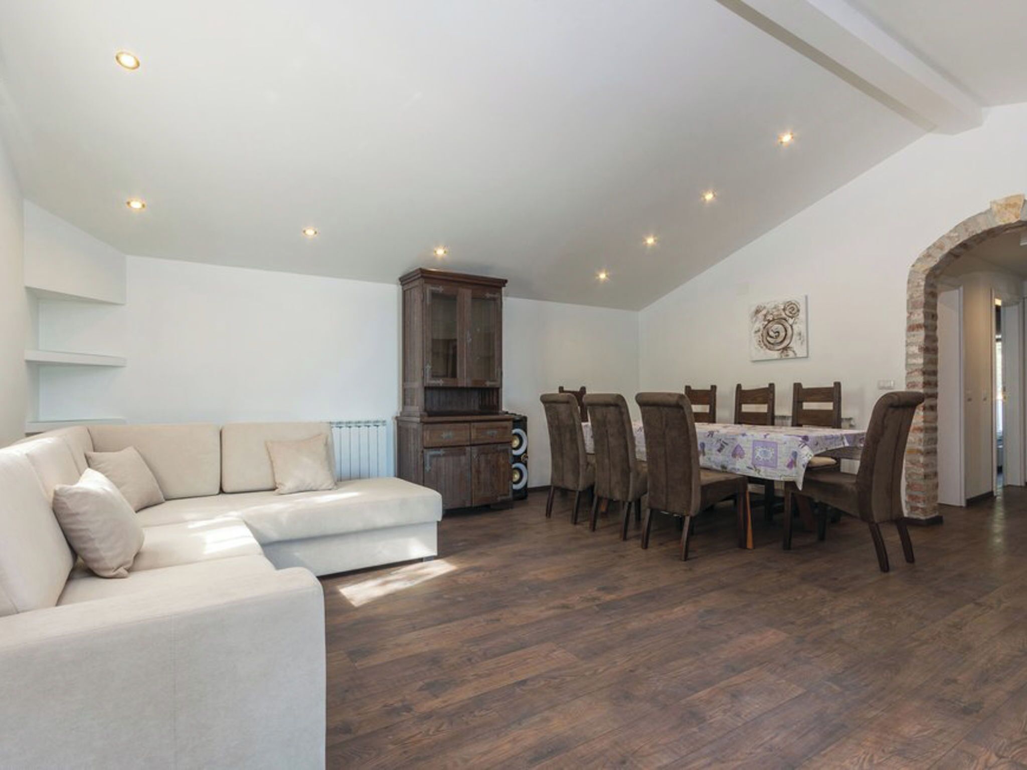 Ein geräumiger Wohnbereich mit einem weißen Sofa, einem Esstisch mit Stühlen und einem Holzkabinett.