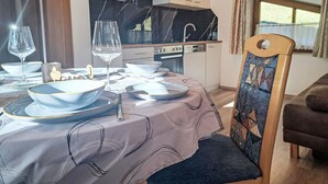 Een eethoek met een gedekte tafel voor twee personen, een keuken op de achtergrond en een uitzicht op de omgeving door een raam.