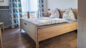 Een slaapkamer met een houten bed, gordijnen met een patroon en een witte bakstenen muur.