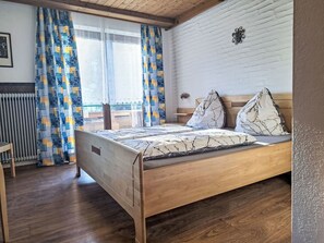 A bedroom with a wooden bed, patterned curtains, and a white brick wall. - Schwarzenegg by Interhome (Wagrain)