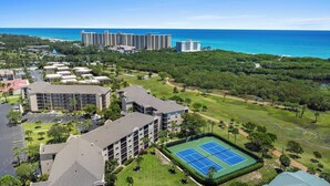 Ett semesterkomplex med flera byggnader, en tennisbana och utsikt över havet.