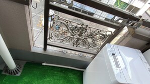 A balcony with a green artificial turf floor, a white air conditioning unit, and a pair of white slippers. - 2 Units Same Floor/30sec Tsutenkaku/1 stop Namba 4 (Naniwa-ku, Osaka City)