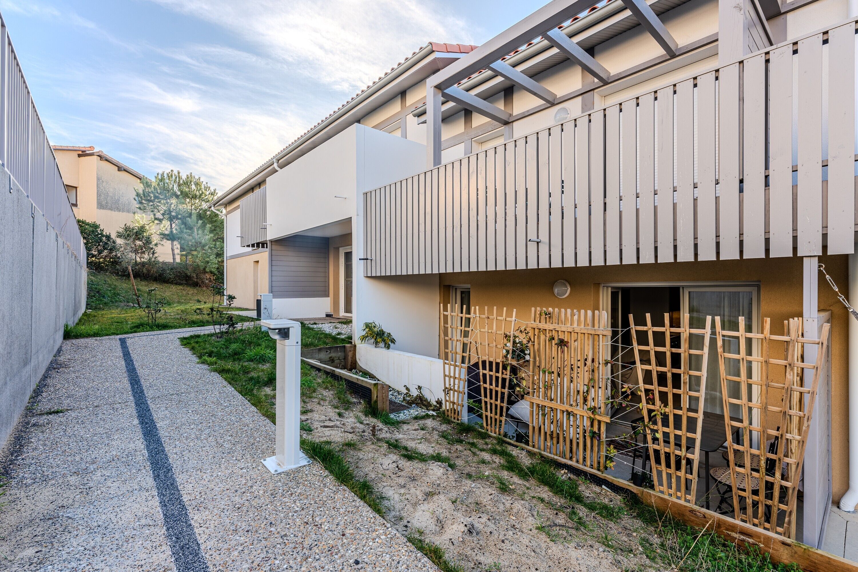 A residential building with a gravel driveway, a wooden fence, and a balcony with a metal railing.