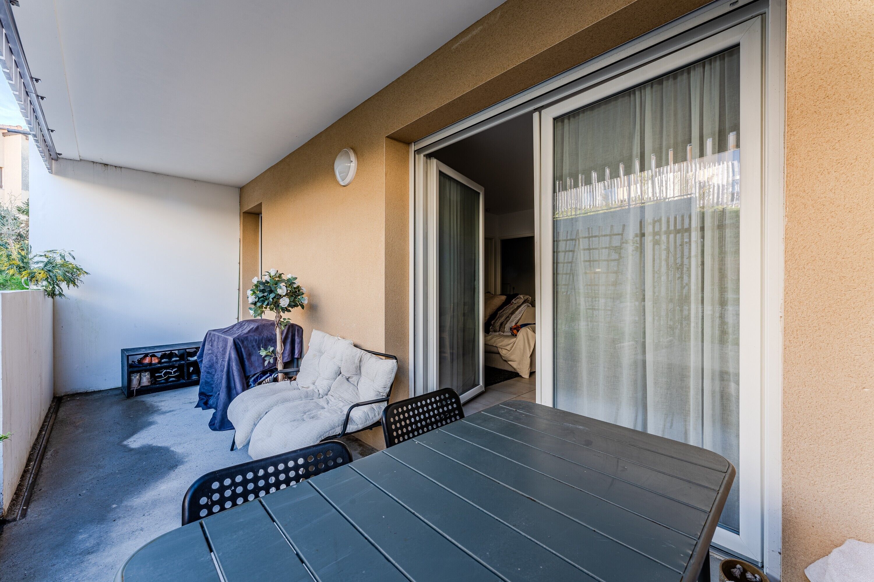 A balcony with a table and chairs, a covered sofa, and a sliding glass door leading to an interior room.