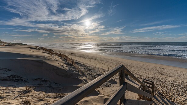 A beach with a wooden walkway leading to the water, a clear sky, and the sun reflecting on the ocean. - “Côté Dunes Mimizan” Apartment – Your Escape Between Ocean and Nature in Mimizan (Mimizan)