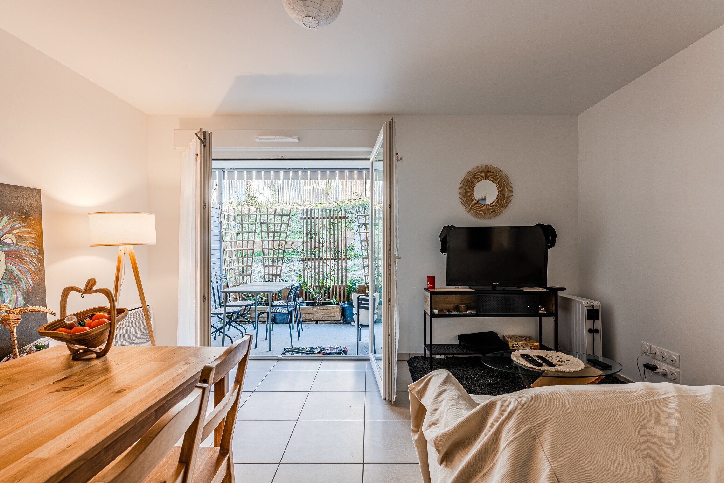 Une pièce comprenant une table à manger en bois, un téléviseur posé sur un meuble, un lit et une vue sur une terrasse extérieure.