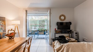 Een kamer met een houten eettafel, een televisie op een dressoir, een bed en uitzicht op een terras.