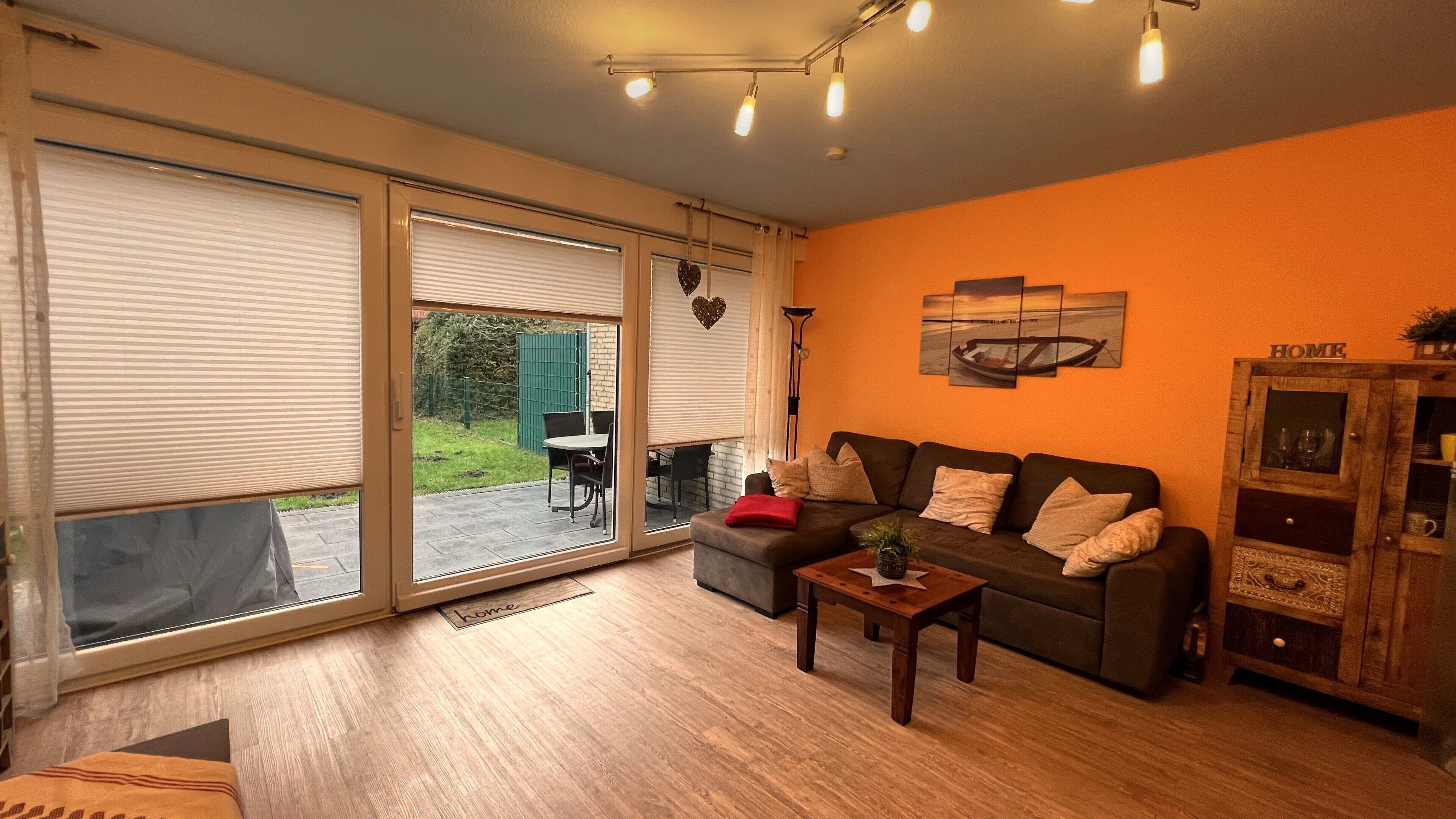 Een woonkamer met een bank, een salontafel en een kast. Er is een schuifdeur naar een buitenruimte met een tafel en stoelen.