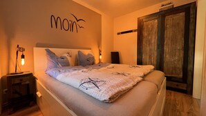 A bedroom with a bed, a nightstand, a wall-mounted light, and a door. - Holiday Apartment Jana (Wangerland)