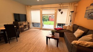 A living room with a sofa, a coffee table, a TV, and a wooden cabinet. - Holiday Apartment Jana (Wangerland)