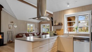 A modern kitchen with a central island, wooden flooring, and a large window providing natural light.