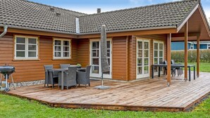 A wooden house with a tiled roof, a covered patio with outdoor furniture, and a barbecue grill.