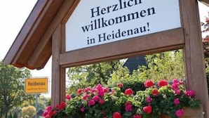 A wooden sign with a crest and the text "Herzlich willkommen in Heidenau!" above a flower box. - Heidenauer Hotel im Park (Heidenau)