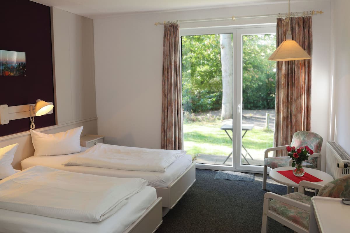 A hotel room with two beds, a chair, a table, and a view of the outdoors.
