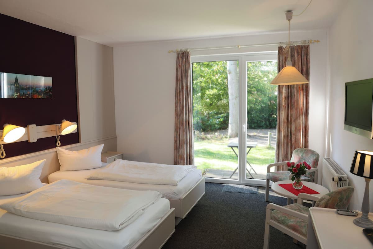 A hotel room with two beds, a desk, a chair, a TV, and a view of the outdoors.