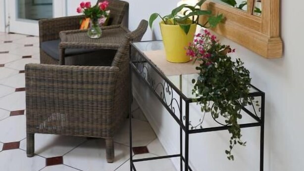 A room with a wicker chair, a small table with a vase and a potted plant, and a large mirror on the wall. - Heidenauer Hotel im Park (Heidenau)