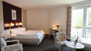 A hotel room with a bed, two chairs, a small table with a bottle and glasses, and a window with curtains. - Heidenauer Hotel im Park (Heidenau)