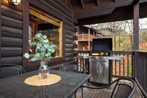 A wooden deck with a grill, a table with a placemat, and a potted plant. - Game Room, Arcade, Theater, Hot Tub • Near Pigeon Forge | Skycrest by AvantStay (Sevierville)