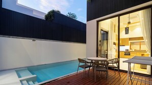 Ein moderner Poolbereich im Freien mit Holzterrasse, Tisch und zwei Stühlen.