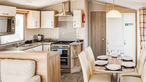 A modern RV kitchen with a dining area, including a stove, oven, sink, and a table set for dining. - Leisure Lodge Hot Tub (Pet) (Potterhanworth)