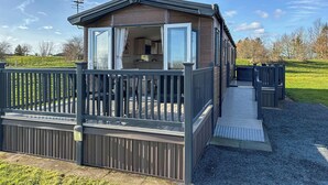 A mobile home with a deck, a small porch, and a visible kitchen area. - Leisure Lodge Hot Tub (Pet) (Potterhanworth)