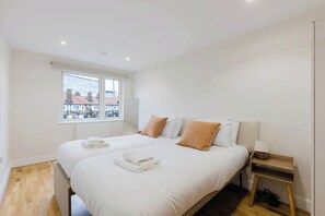 A hotel room with two beds, a window with a view, a bedside table with a lamp, and a pair of shoes on the floor. - Serene Scandi Inspired Flat by Tower Bridge (Greater London)