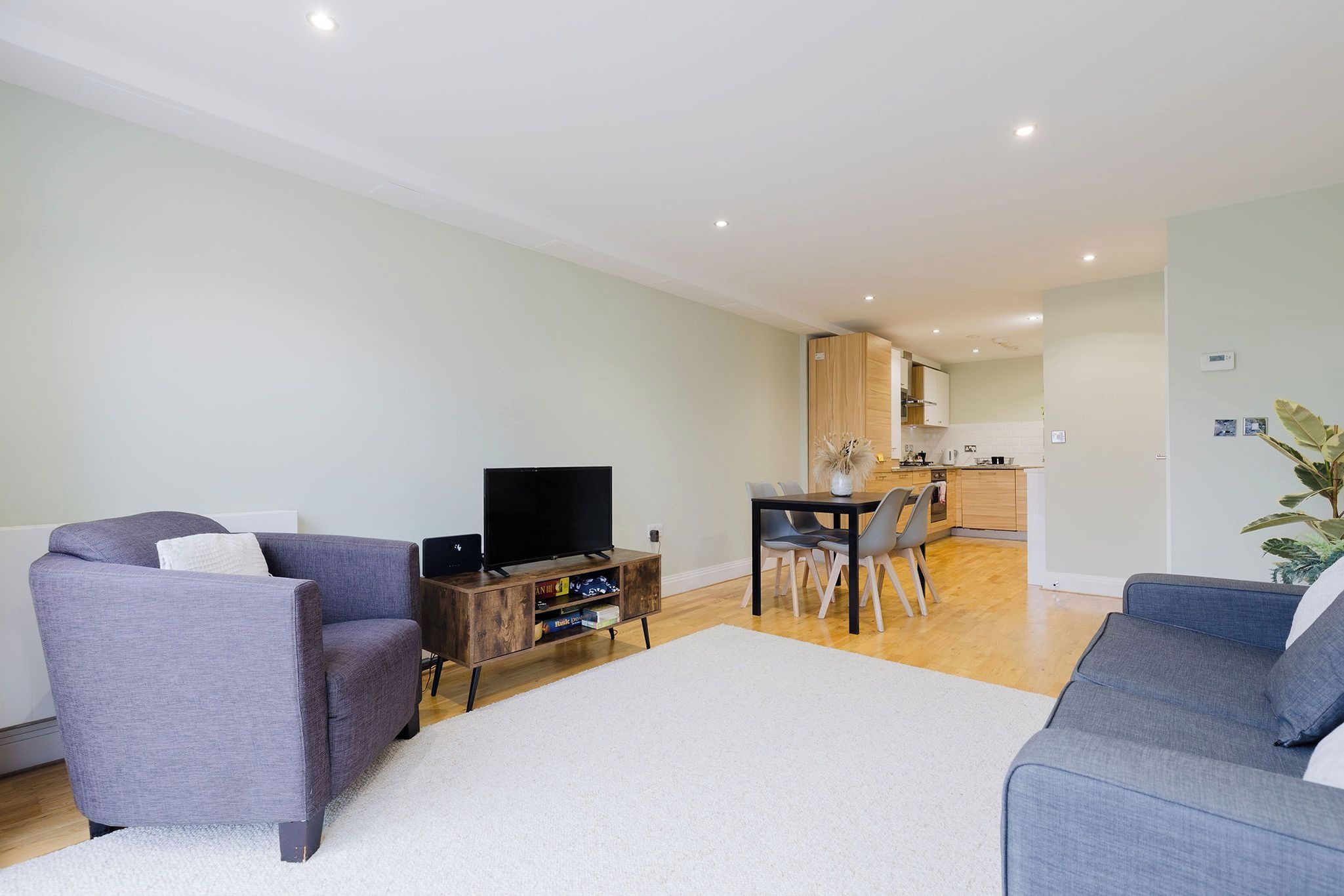 A living room with a sofa, a TV stand, and a dining area with chairs and a table.