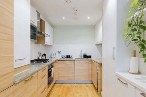 A modern kitchen with wooden cabinets, a stainless steel stove, and a white countertop. - Serene Scandi Inspired Flat by Tower Bridge (Greater London)