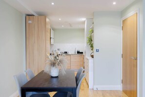 A modern kitchen with white cabinets, a wooden door, and a dining area with a dark table and chairs. - Serene Scandi Inspired Flat by Tower Bridge (Greater London)